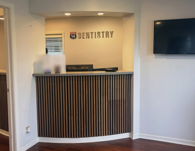 Front desk at Route 14 Dentistry with the practice sign and a wall-mounted TV